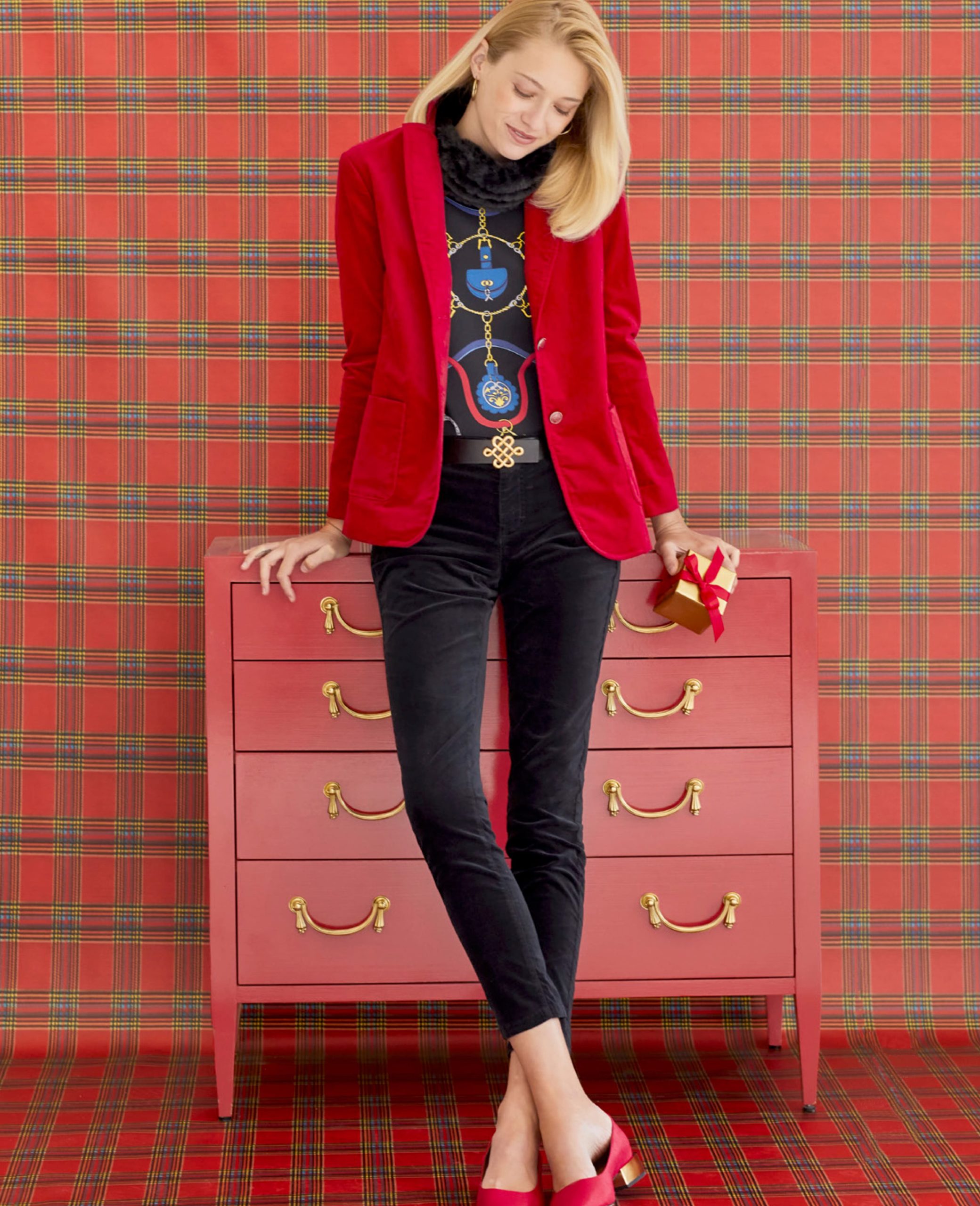 Female model leaning against red dresser in front of plaid wallpapered wall